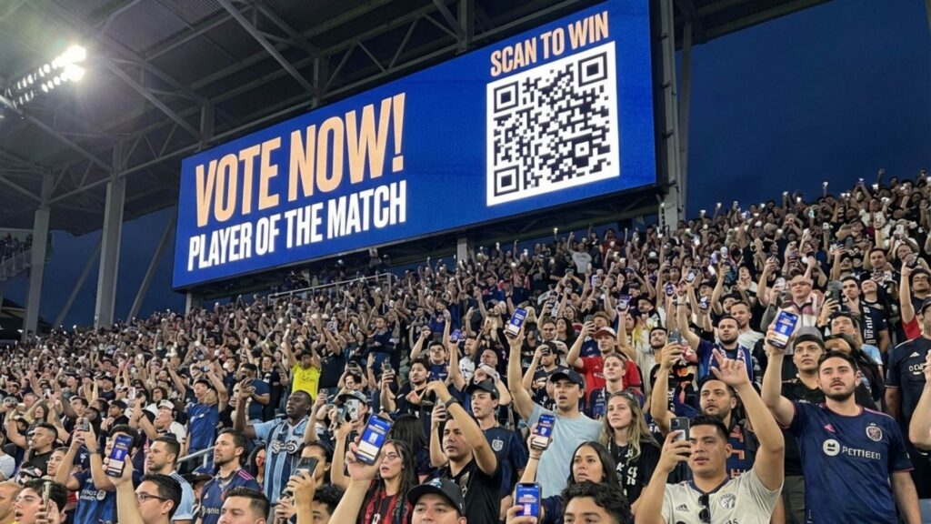 A high-energy crowd with hands in the air, demonstrating the power of live fan engagement software during a stadium event.